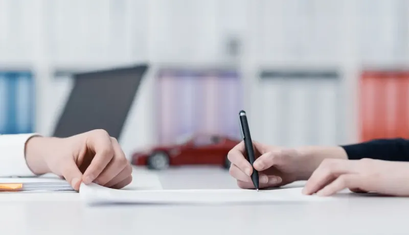 Deux paires de mains sont sur une table, l'une écrivant sur un document, l'autre tenant une feuille.