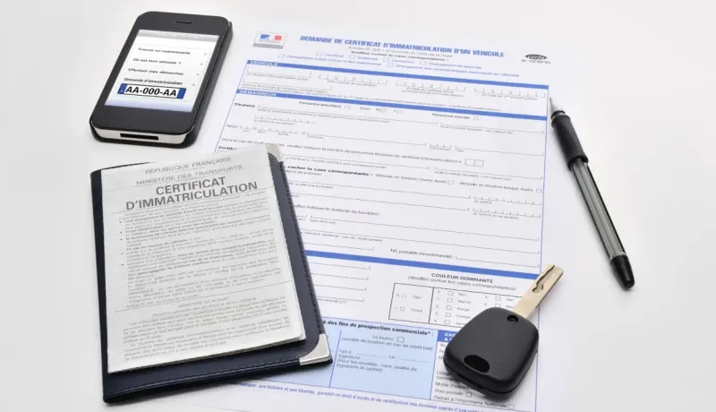 Un certificat d'immatriculation, un téléphone, une clé de voiture et des documents posés sur une table.