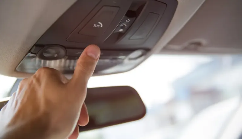 Un doigt appuie sur le bouton "SOS" du panneau de commande au plafond d'une voiture.