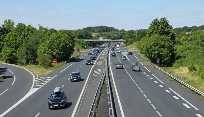 Vue aérienne d'une autoroute française avec plusieurs voitures en mouvement et un pont en arrière-plan.