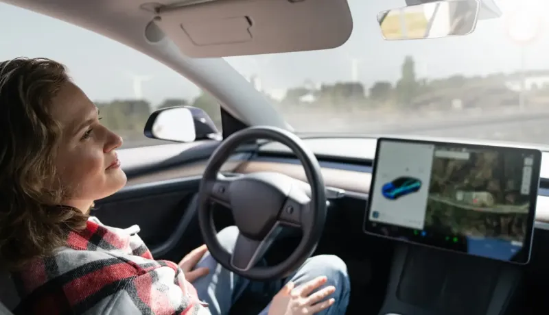 Une jeune femme souriante est assise au volant d'une voiture moderne, regardant le grand écran du tableau de bord.