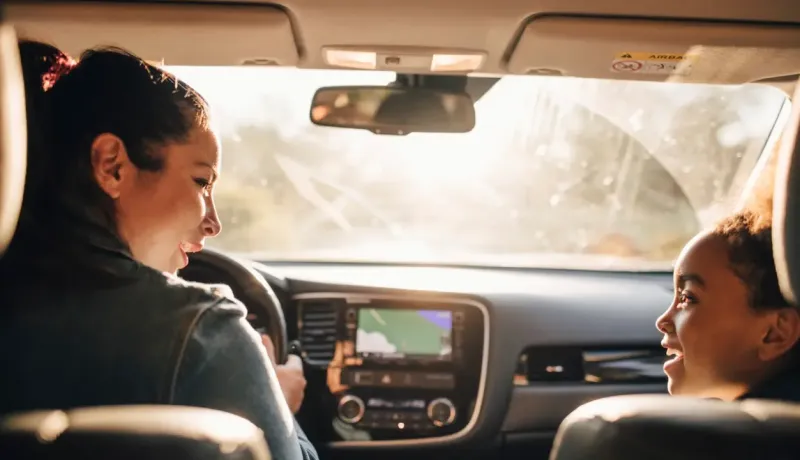 Deux personnes, une femme au volant et une jeune fille à l'arrière, discutent joyeusement dans une voiture.