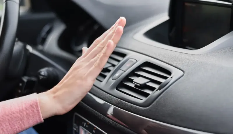 Une main est placée devant la bouche d'aération d'une voiture, vérifiant le flux d'air de la climatisation.
