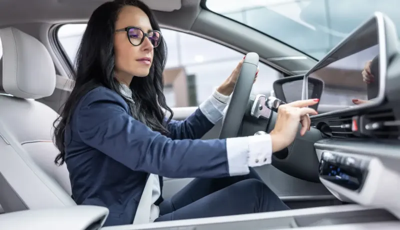 Une femme d'affaires dans une voiture moderne, consultant son tableau de bord avec concentration.