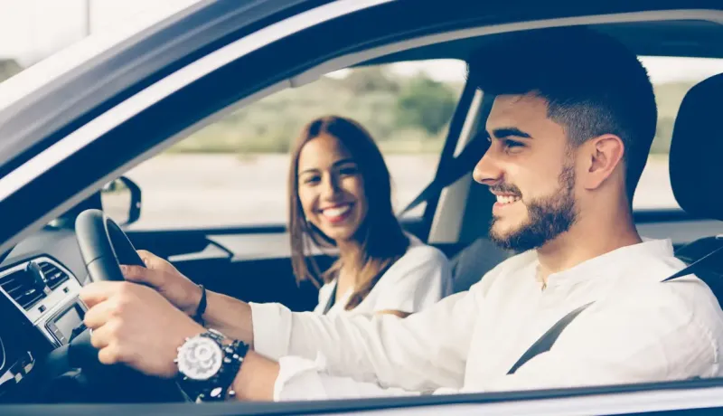 Un homme et une femme souriants à l'intérieur d'une voiture, l'homme au volant.