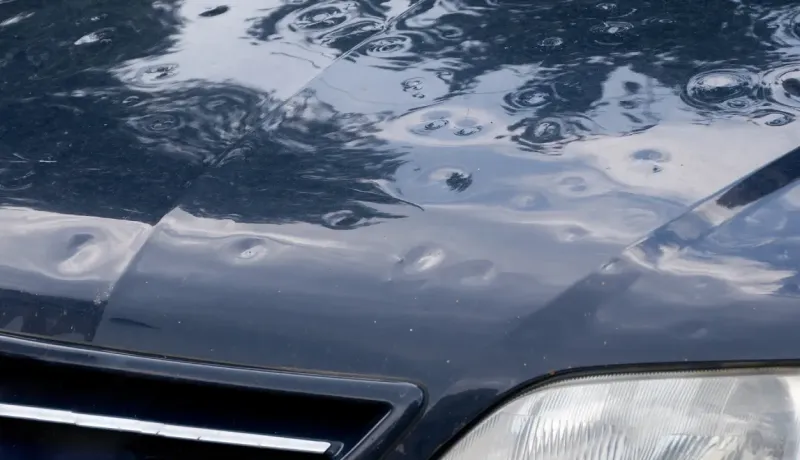 Capot de voiture bleu foncé avec de nombreuses bosses causées par la grêle.
