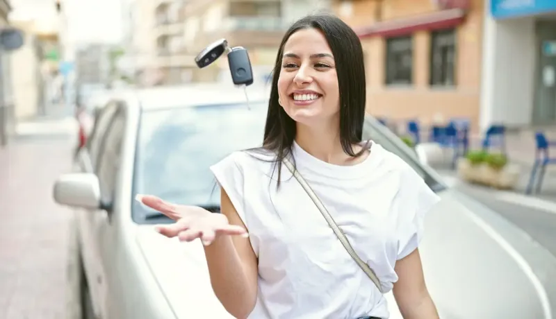 Une femme attrape sa clé de voiture, se tenant devant son véhicule.