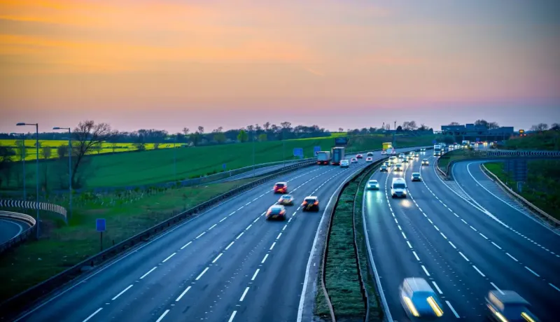 Autoroute très fréquentée au coucher du soleil avec des champs verts à l'arrière-plan.