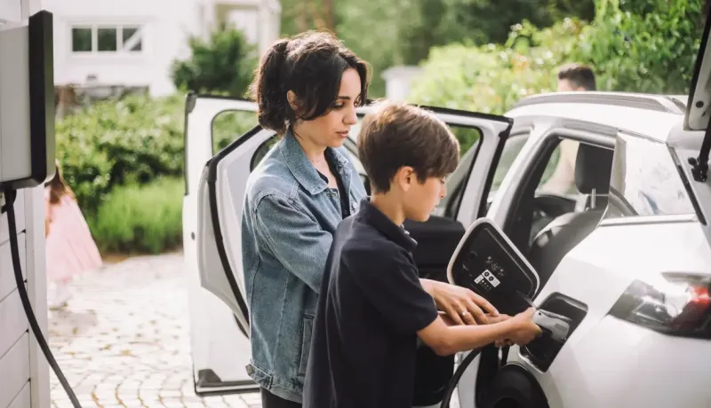 Une mère aide son fils à brancher la voiture électrique devant la maison.