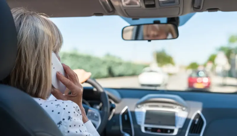 Une femme conduit une voiture tout en parlant au téléphone, vue de l'arrière.