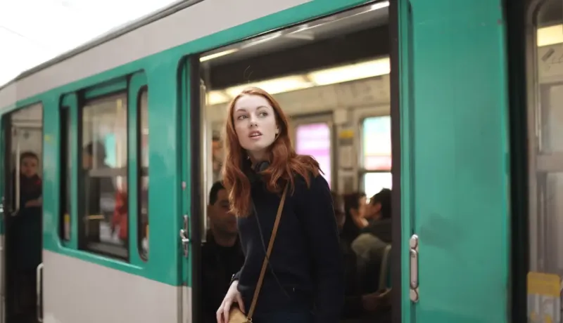 Une jeune femme aux cheveux roux regarde par la porte ouverte d'un metro à l'arrêt.