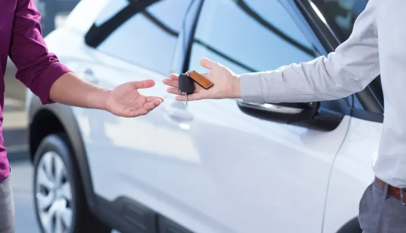 Des mains échangeant les clés d'une voiture blanche, symbolisant une location ou une vente.