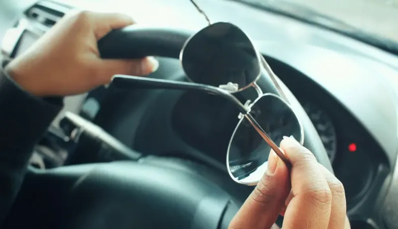 Gros plan sur des mains tenant des lunettes de soleil au-dessus d'un volant de voiture.