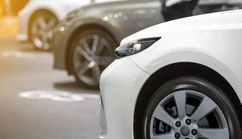 Gros plan sur l'avant d'une voiture blanche garée, avec d'autres véhicules flous derrière.