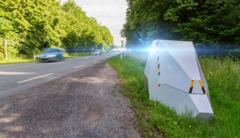 Un radar automatique sur le bord d'une route verdoyante, flashant une voiture en mouvement.