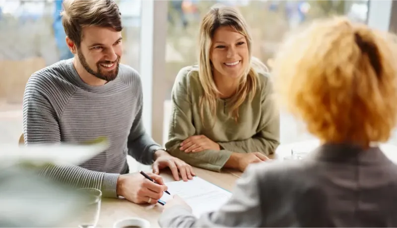 Un couple souriant signe des documents avec un conseiller financier.