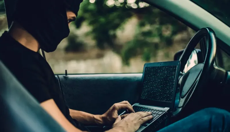 Un homme masqué tapant sur un ordinateur portable à l'intérieur d'une voiture.