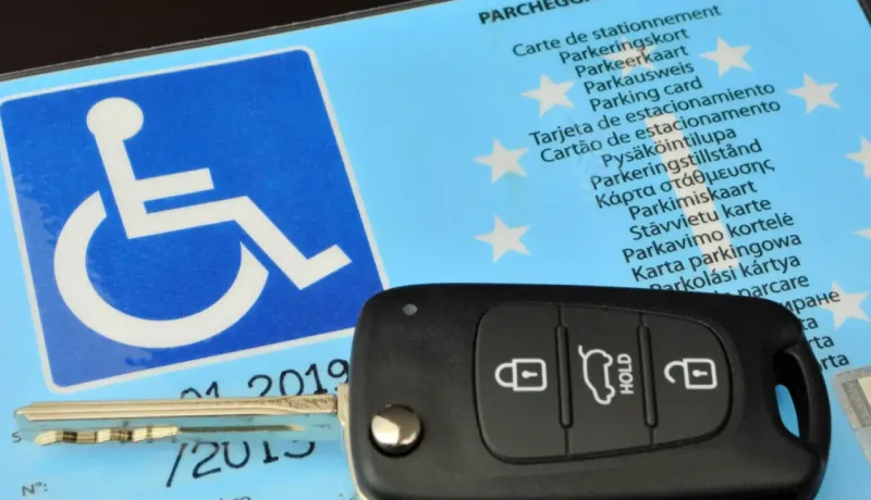 Carte de stationnement pour personne handicapée et clé de voiture sur un fond bleu.