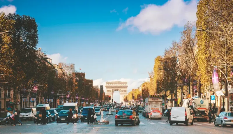 Vue large des Champs-Élysées animés à Paris, avec l'Arc de Triomphe en arrière-plan sous un ciel bleu.