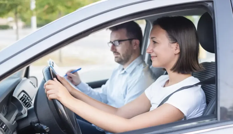 Jeune femme souriante apprenant à conduire avec un instructeur attentif dans une voiture.