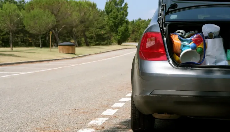 Le coffre d'une voiture grise rempli de sacs et d'articles, garée sur le côté d'une route.