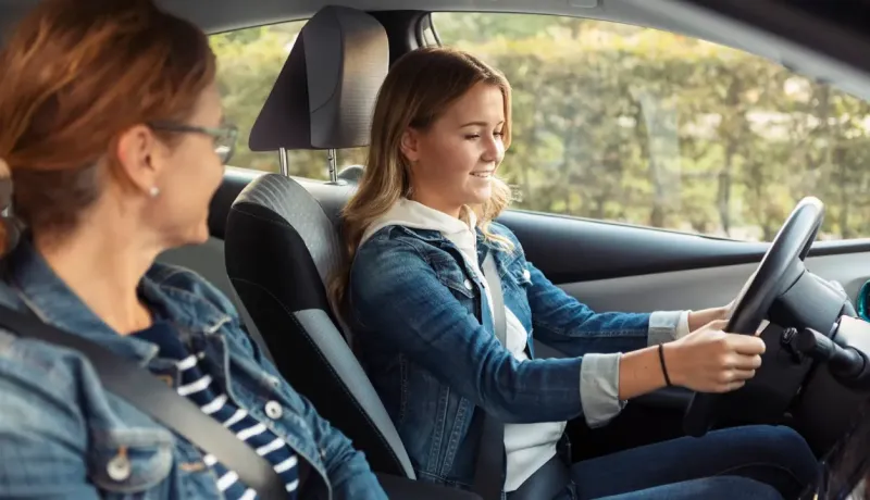 Une mère apprend à sa fille à conduire un véhicule.