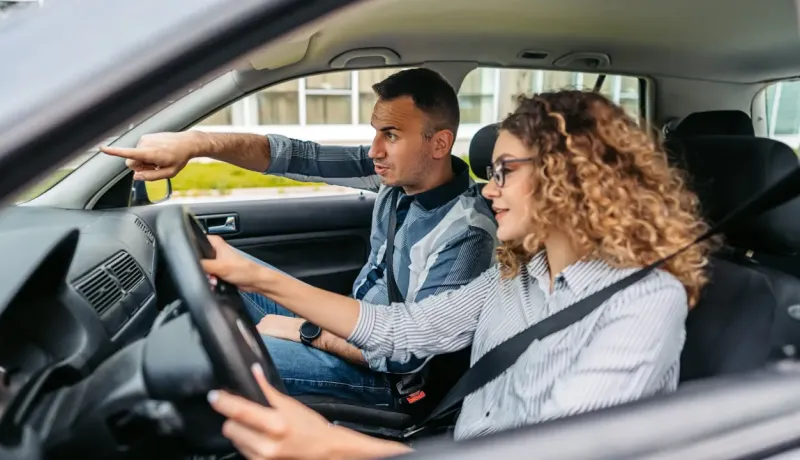 Un homme montre une direction à une jeune femme au volant d'une voiture.