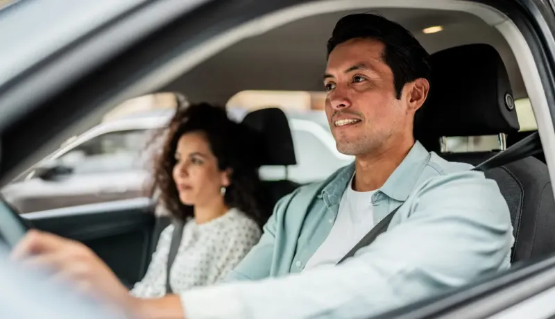 Un homme au volant d'une voiture, sa femme assise à côté de lui.