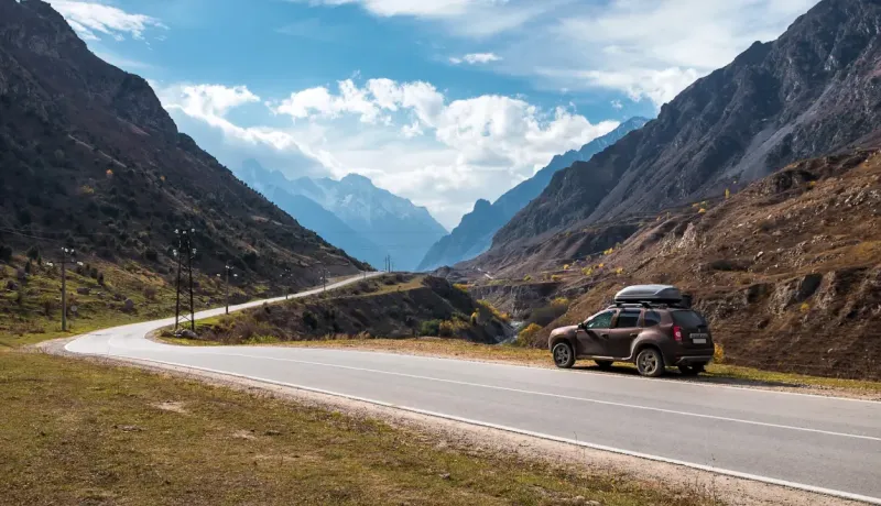 Un SUV marron avec un coffre de toit garé sur le bord d'une route sinueuse au milieu de montagnes imposantes.