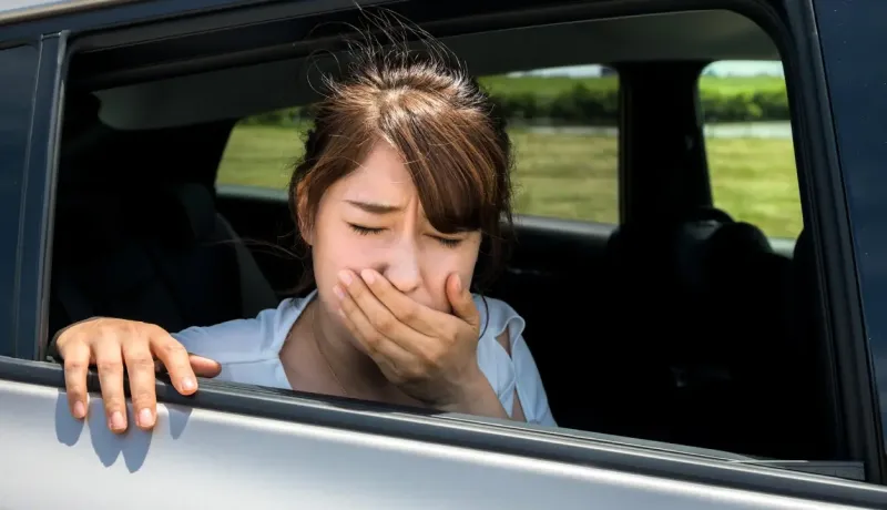 Une jeune femme dans une voiture, la main devant la bouche, l'air nauséeux ou malade.