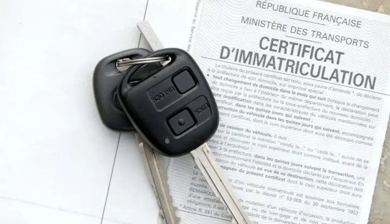 Une clé de voiture noire est posée sur un document officiel français : un certificat d'immatriculation.