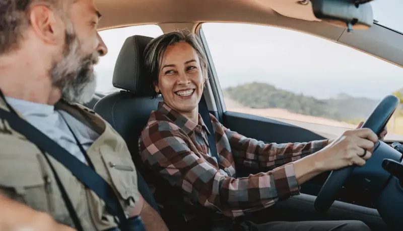 Un couple souriant conduisant une voiture.