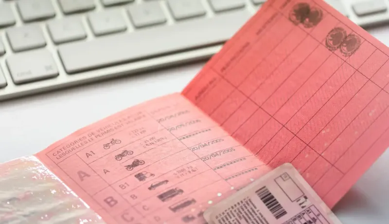 Gros plan d'un permis de conduire français en papier rose, avec une partie de clavier en arrière-plan.