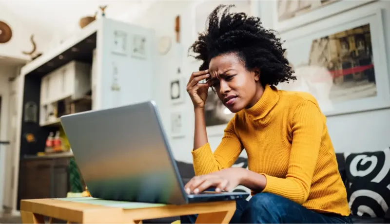 Une jeune femme, l'air stressé, regarde son ordinateur portable à la maison.