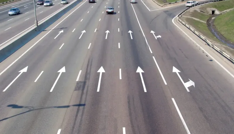 Vue aérienne d'une autoroute à plusieurs voies avec des flèches directionnelles peintes sur l'asphalte.