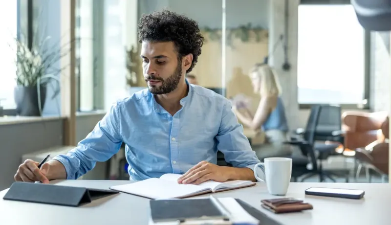 Un homme à son bureau, concentré sur sa tablette dans un environnement de bureau moderne.