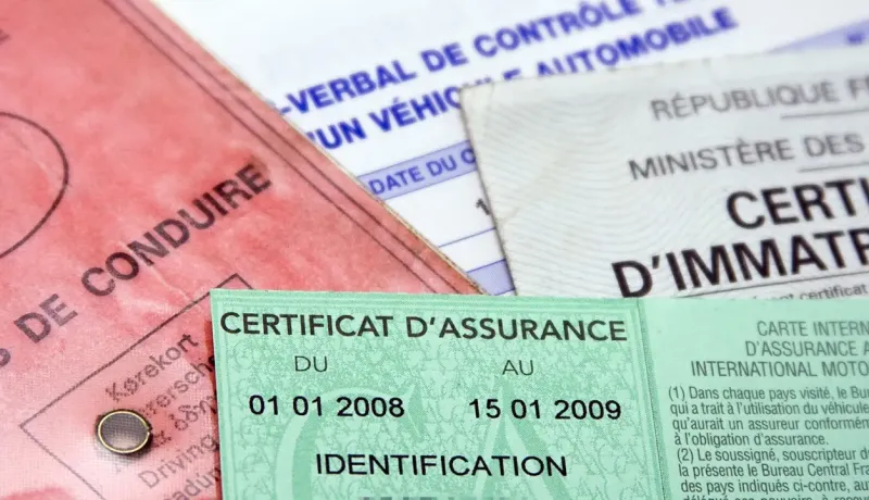 Gros plan sur des documents officiels, dont un "Certificat d'Assurance" vert et un permis de conduire.