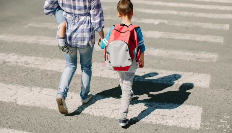 Une femme et un enfant traversent une route sur un passage piéton en plein soleil.