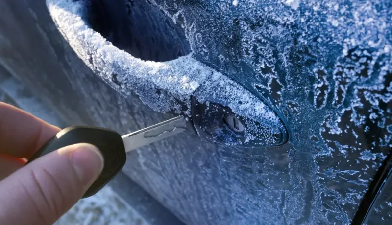 Une main insère une clé dans la serrure d'une portière de voiture givrée par le gel.