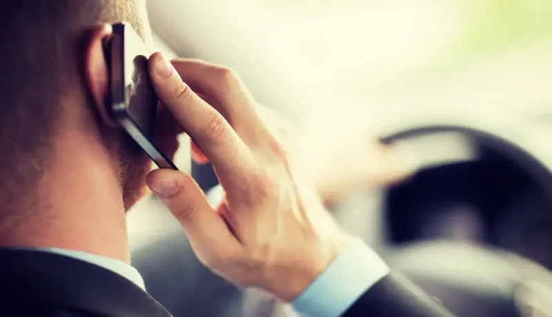 Vue arrière d'un homme en costume tenant un téléphone portable à son oreille en conduisant.