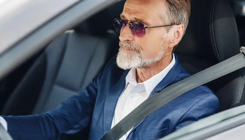 Un homme élégant, âgé, avec une barbe blanche et des lunettes de soleil, est assis dans une voiture.