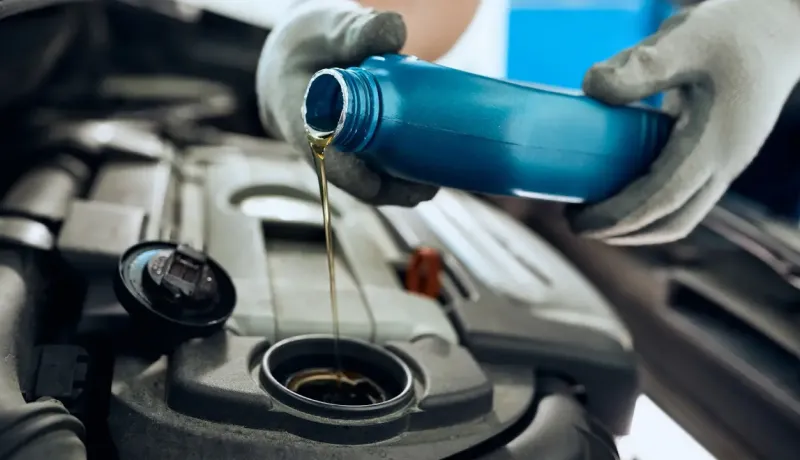 Un mécanicien en gants de travail verse de l'huile neuve dans le moteur d'une voiture.