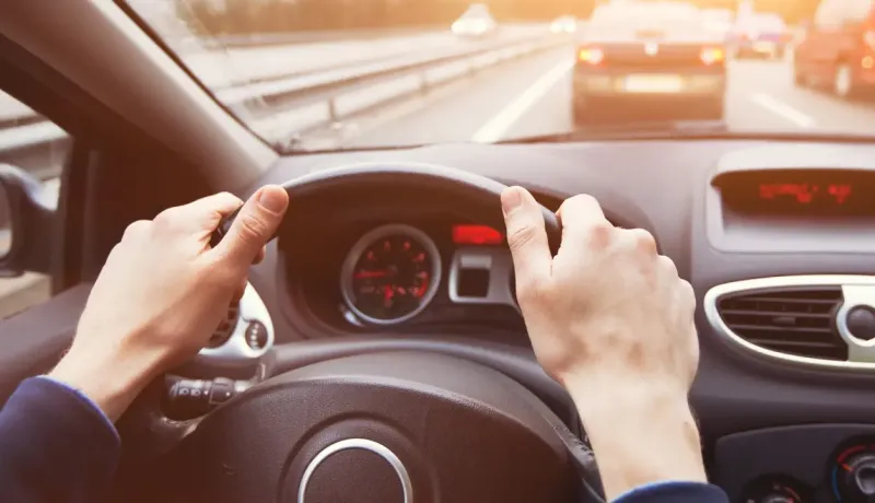 Vue subjective d'une personne conduisant une voiture sur une autoroute encombrée au lever du soleil.