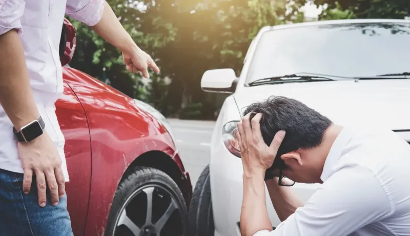 Deux hommes confrontent après un accident de voiture. L'un, en t-shirt rose, pointe du doigt un autre, désespéré, en t-shirt blanc.