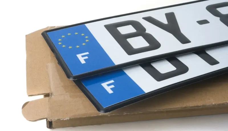Deux plaques d'immatriculation françaises neuves avec le drapeau de l'UE et la lettre 'F', sur une boîte.