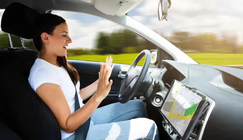Une femme souriante dans une voiture avec les mains levées, utilisant un écran de navigation.
