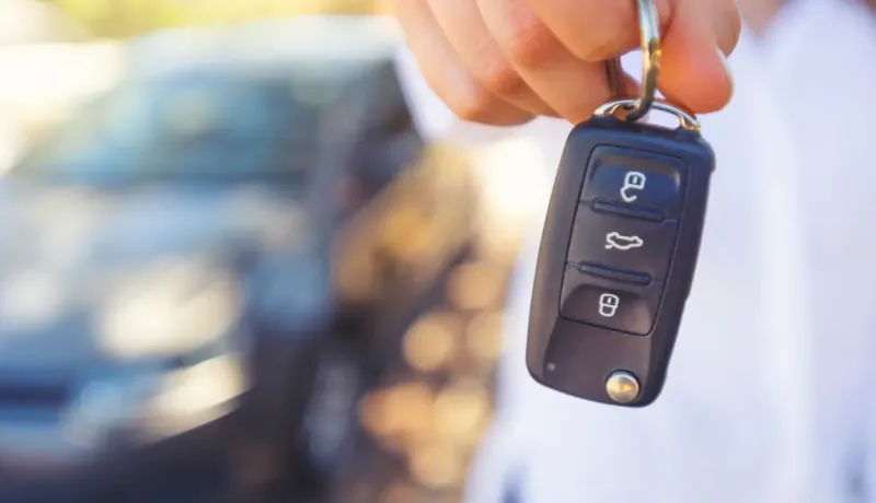 Une main tend une clé de voiture moderne avec télécommande, avec une voiture floue en arrière-plan.