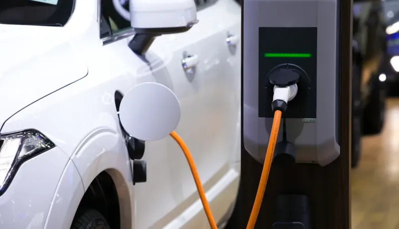 Gros plan d'une voiture électrique blanche en charge à une borne avec un câble orange.