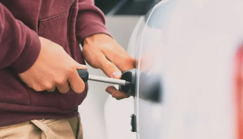 Gros plan de mains manipulant un tournevis pour ouvrir une poignée de portière de voiture blanche.