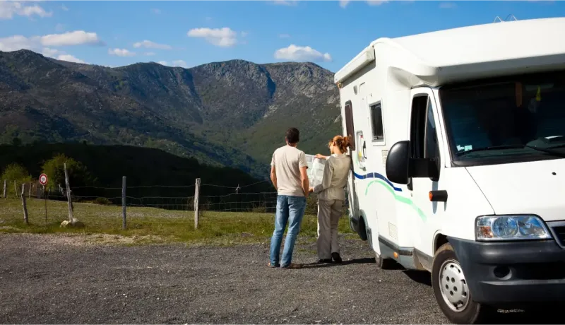 Un couple regarde un paysage montagneux impressionnant à côté de leur camping-car blanc garé sur le bord d'une route.